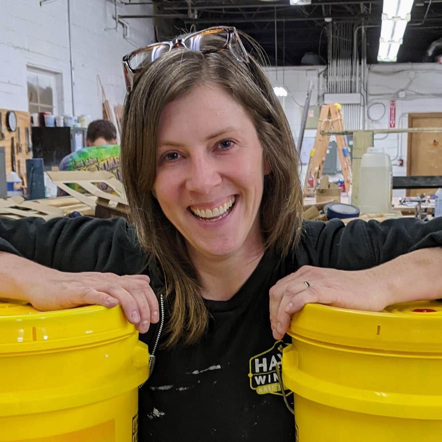 Colorful workshop with a smiling woman leaning on yellow buckets, showcasing professional window restoration at Hayes Window Restoration.