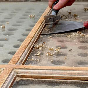 Old window frame restoration process with scraping tools on wooden frame.