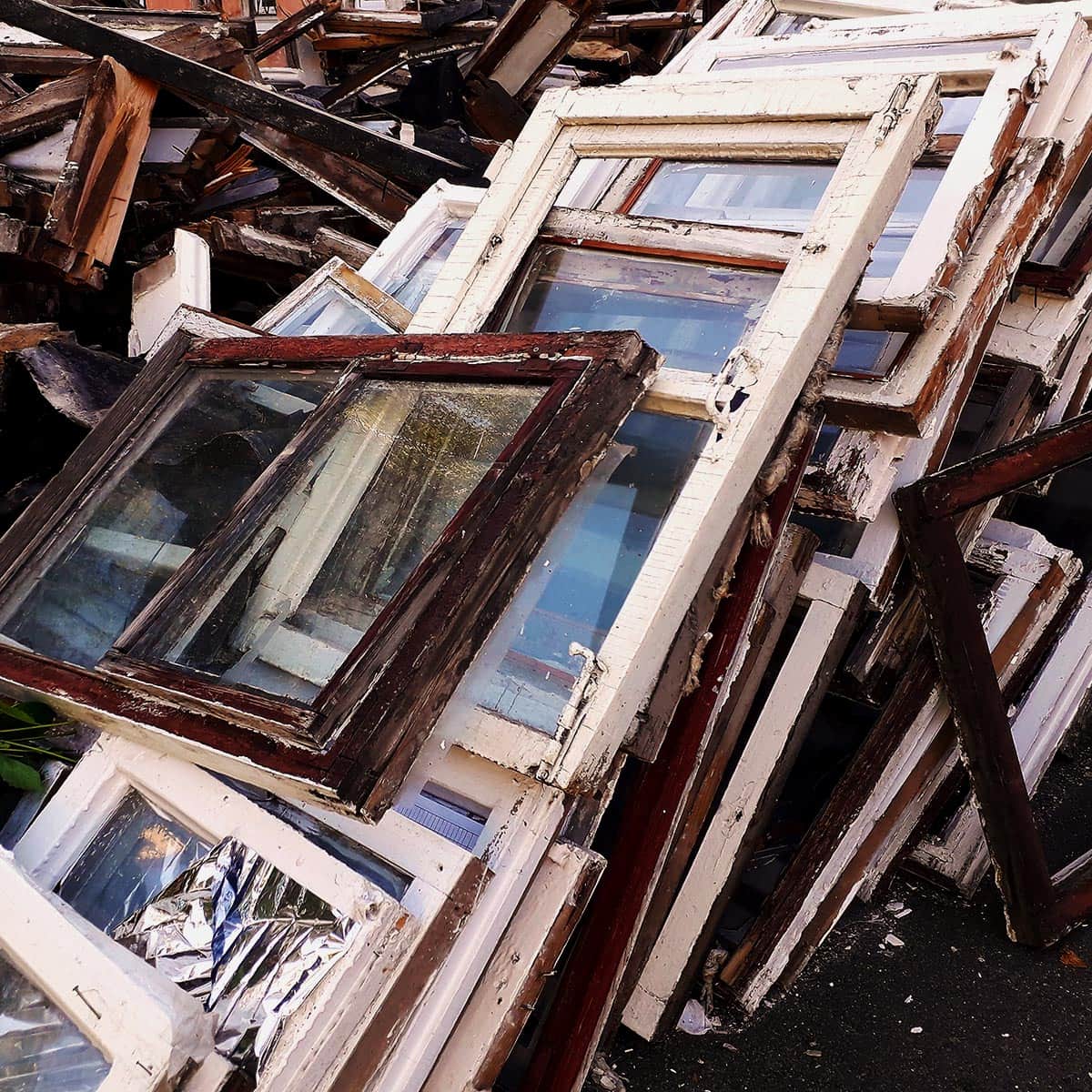 Broken and weathered window frames stacked together, awaiting restoration or recycling.