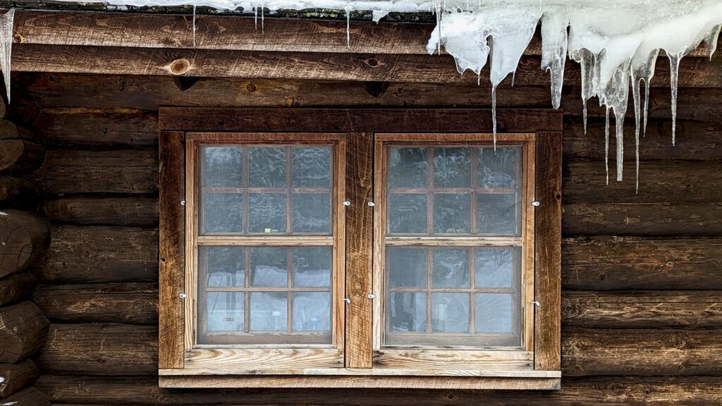 Weathered wooden window with ice and snow on log cabin exterior during winter restoration.